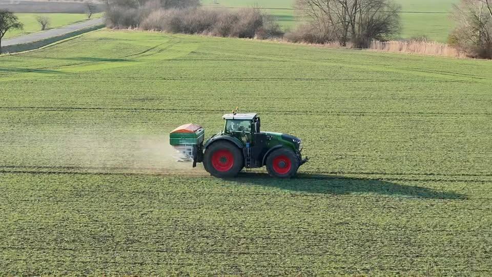 Traktor Fendt s rozmetadlem hnojiv přihnojuje zelenou pšenici.